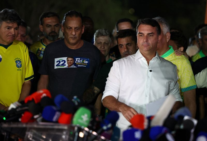 Flávio Bolsonaro stands at a row of microphones after the presidential runoff.