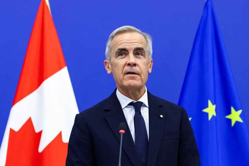 Mark Carney stands between Canadian and European Union flags at a press conference.