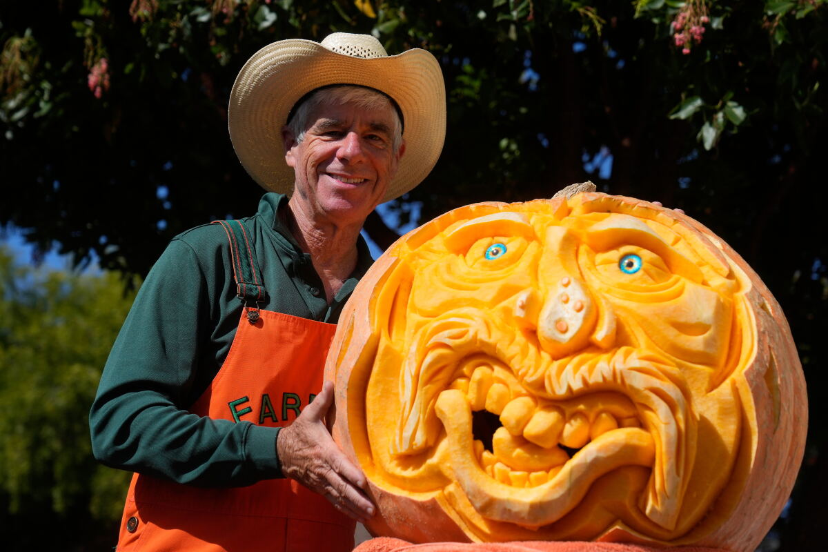 Farmer Mike Valladao beside a giant pumpkin carved into an expressive face.